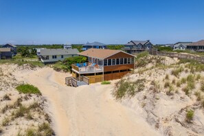 A beachfront property with a large house featuring a deck and a sandy path leading to it.