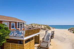 A beachfront property with a wooden deck, a covered seating area, and a view of the ocean.