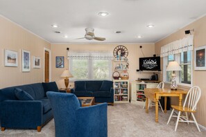 Uma sala de estar com sofá azul, mesa de centro, televisão, estante de livros e área de jantar com mesa e cadeiras.