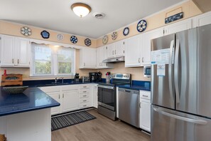 Cozinha com armários brancos, eletrodomésticos de aço inoxidável, bancada azul e pratos decorativos na parede.