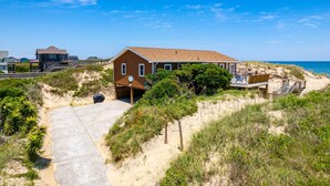 Une propriété située en bord de mer, comprenant une maison principale, une terrasse couverte et un chemin de sable menant à la plage.