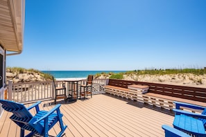 Um deck de madeira com cadeiras azuis e uma mesa, com vista para uma praia.