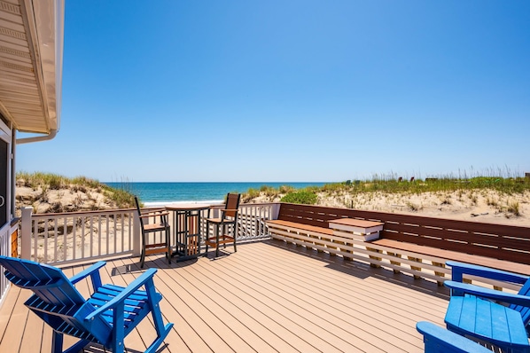 A wooden deck with blue chairs and a table overlooking a beach.