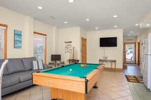 A living room with a pool table, a sofa, a television, and a door leading to the outside.