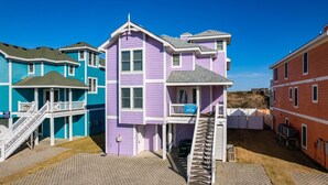 A multi-story building with a purple exterior, a balcony, and a staircase leading to the upper floor. - Celestial Shore-Oceanfront, pool, hot tub, elevator, rec room & dog friendly! (Nags Head)