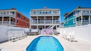 A swimming pool with lounge chairs and a barbecue area, surrounded by multi-story buildings with balconies. - Celestial Shore-Oceanfront, pool, hot tub, elevator, rec room & dog friendly! (Nags Head)