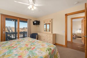 Ein Schlafzimmer mit Bett, Kommode, Fernseher und Balkontür.