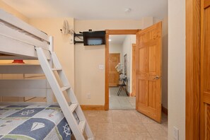 Una cama litera con escalera, un ventilador montado en la pared y una puerta que da a una habitación con una silla y una mesa.