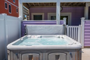 A hot tub with a white cover, set against a purple building with a white fence.