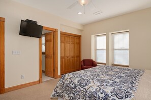 A bedroom with a bed, a TV mounted on the wall, a closet, and a chair.