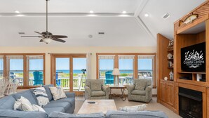 A spacious living room with a gray sectional sofa, two armchairs, a coffee table, and a fireplace. Large windows offer a view of the ocean. - Celestial Shore-Oceanfront, pool, hot tub, elevator, rec room & dog friendly! (Nags Head)