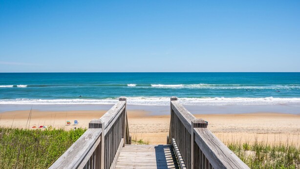 A wooden boardwalk leading to a beach with clear blue water and a sandy shore. - Celestial Shore-Oceanfront, pool, hot tub, elevator, rec room & dog friendly! (Nags Head)