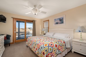 A bedroom with a bed, a nightstand, a dresser, a ceiling fan, a window with blinds, and a door leading to a balcony.