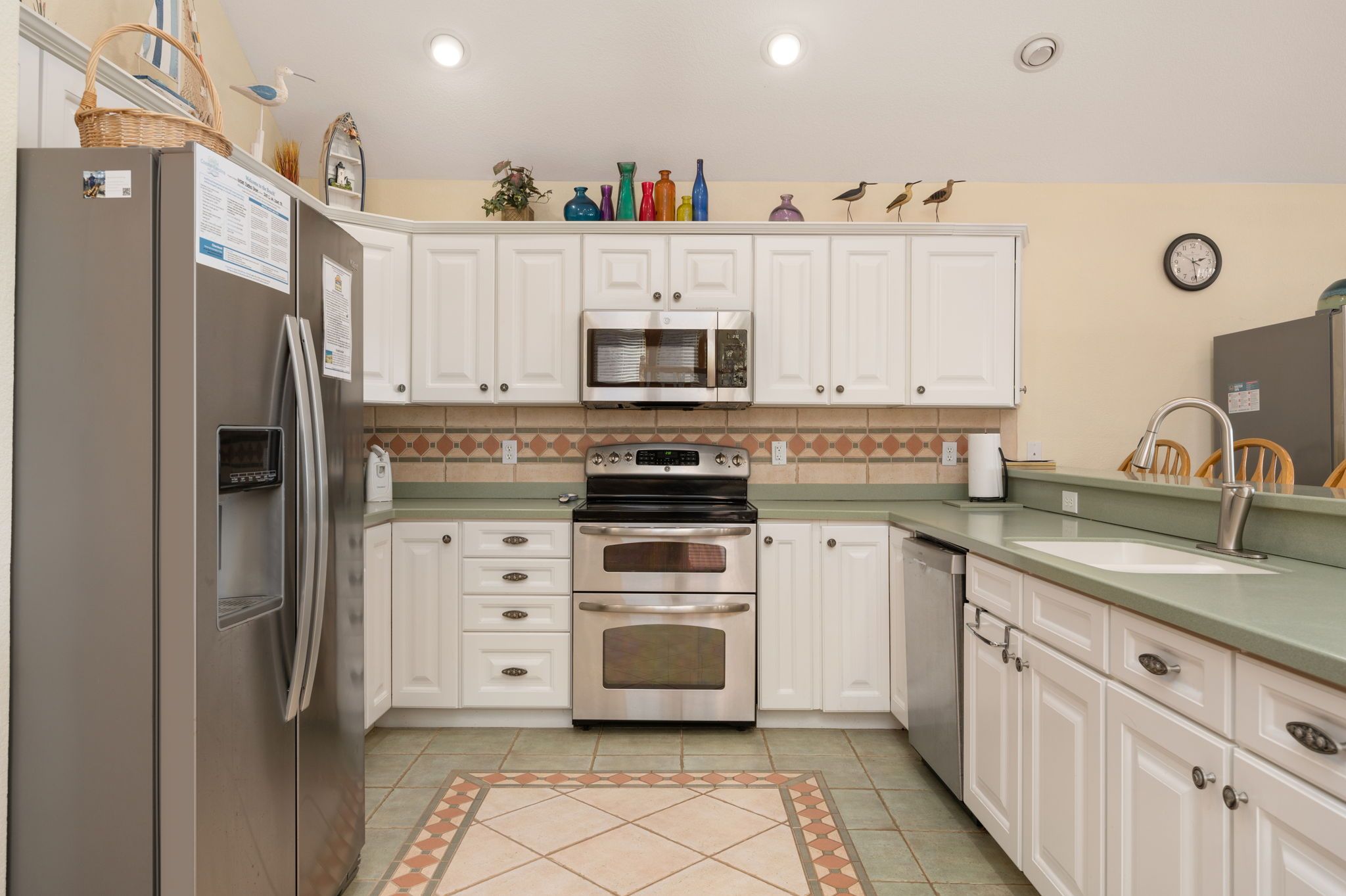 A kitchen with white cabinets, a stainless steel refrigerator, a microwave, an oven, and a sink.
