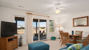 Ein Wohnzimmer mit Fernseher, blauem Sofa, Korbsesseln und Deckenventilator.