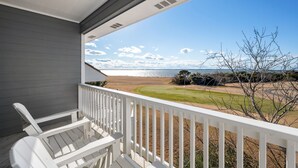 Ein Balkon mit weißen Geländern, der auf einen Strand und einen Golfplatz blickt.