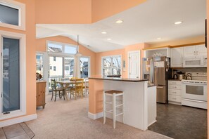 A kitchen with white cabinets, a stainless steel refrigerator, and an oven. There is a dining area with a table and chairs.