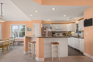 A modern kitchen with white cabinets, a central island, and a dining area with a table and chairs.