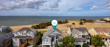 A coastal residential area with houses near the beach, a golf course, and a body of water.