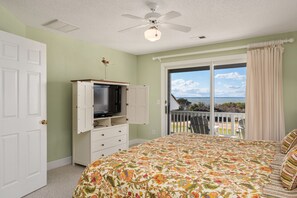 A bedroom with a large bed, a television on a cabinet, and a balcony with a view. - Sound View: Soundfront, water, golf course & great sunset views, community pool! (Nags Head)