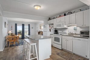 A modern kitchen with white cabinetry, a central island, and a dining area with wooden chairs and a table.
