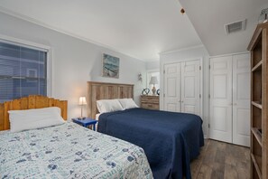 Un dormitorio con dos camas, un cabecero de madera, una mesita de noche con una lámpara y un cuadro en la pared.