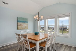 A dining room with a wooden table and white chairs, a chandelier, and a painting on the wall.