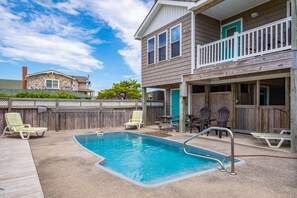 A backyard with a swimming pool, lounge chairs, and a wooden deck.