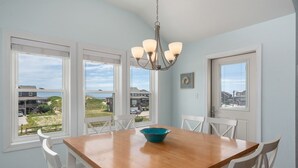 Uma sala de jantar com uma mesa de madeira, cadeiras brancas, uma tigela azul e um lustre.