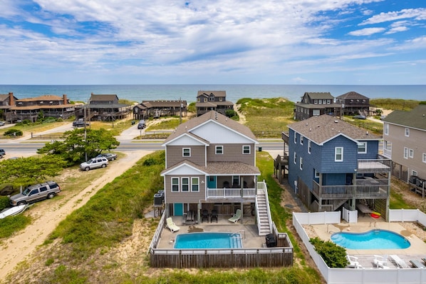 Un quartier résidentiel situé sur la côte, avec des maisons, une piscine et une plage en arrière-plan.