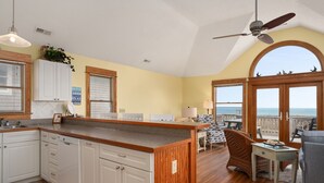 A spacious kitchen with wooden cabinets, a central island, and a view of the ocean through large windows. - Sea Rest: Oceanfront, private walkway to beach, hot tub, YMCA access. (Nags Head)