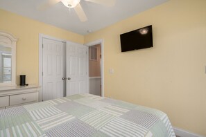 Une chambre à coucher avec un lit, une commode, un miroir, un ventilateur de plafond et un téléviseur fixé au mur.