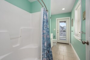 A bathroom with a shower, toilet, and a door leading outside.