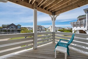A wooden deck with a bench and railing, overlooking a residential area with houses.