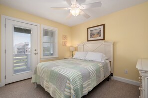 Une chambre à coucher avec un lit, un ventilateur de plafond, une porte avec des stores et un mur orné de deux tableaux encadrés.