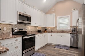 A kitchen with white cabinets, stainless steel appliances, a microwave, a stove, and a refrigerator.
