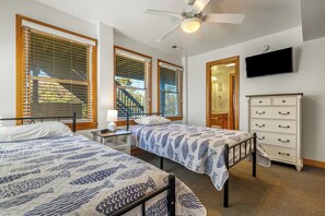 Un dormitorio con dos camas, ventilador de techo, televisión y cómoda.