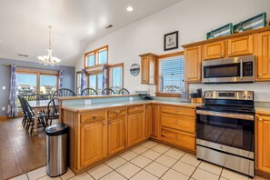 A modern kitchen with wooden cabinets, stainless steel appliances, and a dining area with a chandelier. - Our Happy Place: Oceanside, private and community pool, hot tub, dog friendly (Nags Head)