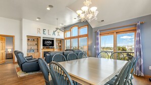 Un vaste espace dédié à la salle à manger, avec une grande table et des chaises, un ventilateur de plafond et une vue sur l’extérieur grâce à de grandes fenêtres.