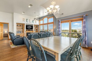 Un comedor amplio con una mesa grande y sillas, un ventilador de techo y vistas al exterior a través de ventanas grandes.
