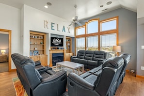 A spacious living room with leather recliners, a fireplace, and a large window with blinds.