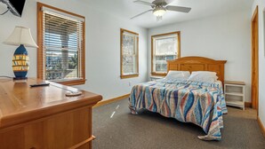 Une chambre à coucher avec un lit, un bureau avec une lampe et un ventilateur de plafond.