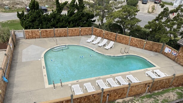 Une piscine entourée d’une terrasse en briques, de chaises longues et d’une clôture en bois.