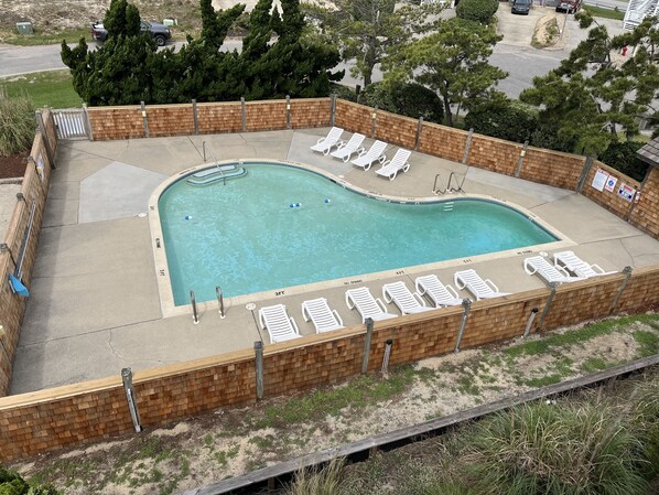 Una piscina con solárium de ladrillo, rodeada de sillones de descanso y una cerca de madera.