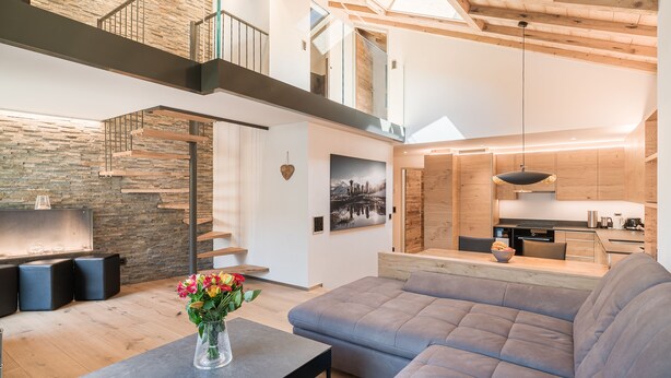 Un interior moderno con una escalera de madera, un sofá gris y un comedor.