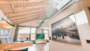 Una sala de estar moderna con techo de madera, un ventanal grande y un cuadro de un paisaje nevado.