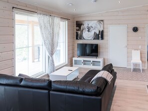 A modern living room with a black leather sofa, a white coffee table, a flat-screen TV, and a painting on the wall.