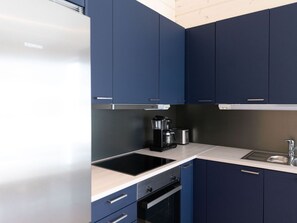 A modern kitchen with dark blue cabinets, a stainless steel refrigerator, a coffee maker, and a built-in oven. - Saana 4 by Interhome (Enontekiö)