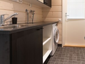 Une cuisine compacte équipée d’un lave-linge intégré, d’un évier avec robinet et d ’une fenêtre avec stores.