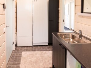 A compact kitchen with a stainless steel sink, a white refrigerator, and a dark wooden cabinet. - Saana 4 by Interhome (Enontekiö)
